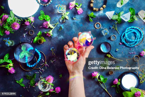 hand holding stylish pink kaleidoscope sunglasses with gold bracelets and rings in a feminine style concept with clover flowers on a dark background. beautiful summer accessories. - khabarovsk krai stock pictures, royalty-free photos & images