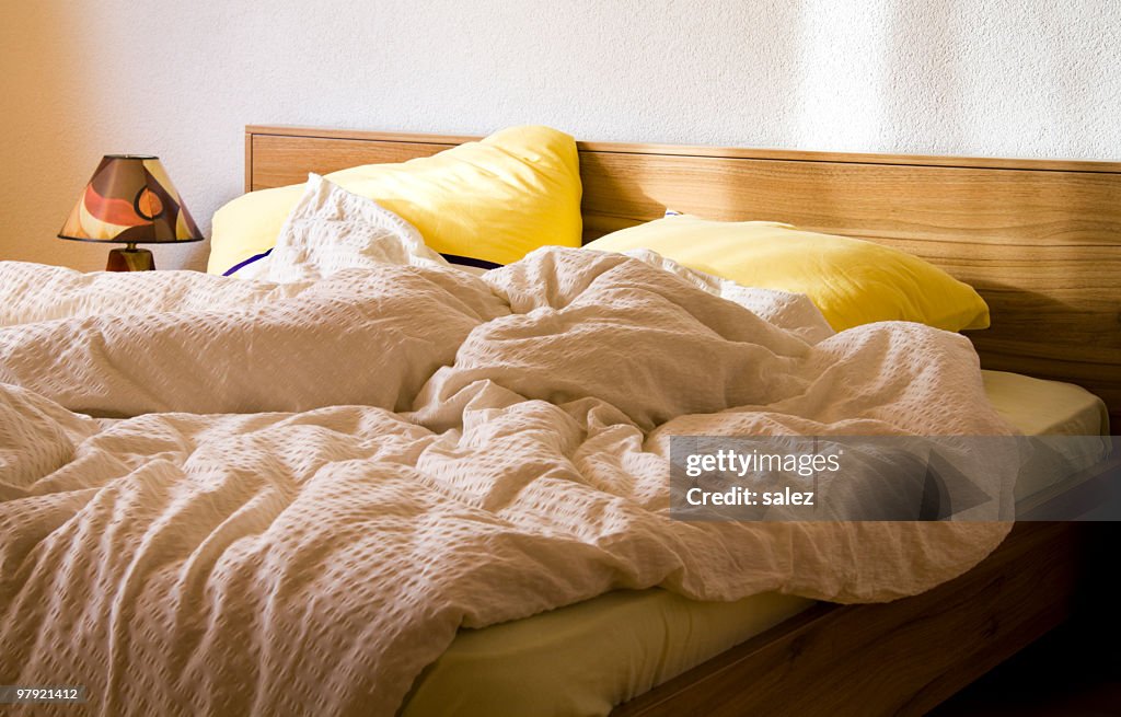 An unmade bed with yellow pillows in the morning
