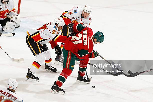 Kyle Brodziak of the Minnesota Wild battles for control of a loose puck with Steve Staios and Jay Bouwmeester of the Calgary Flames during the game...