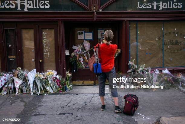 Woman takes a photograph of flowers, notes and photographs left in memory of Anthony Bourdain at the closed location of Brasserie Les Halles where...