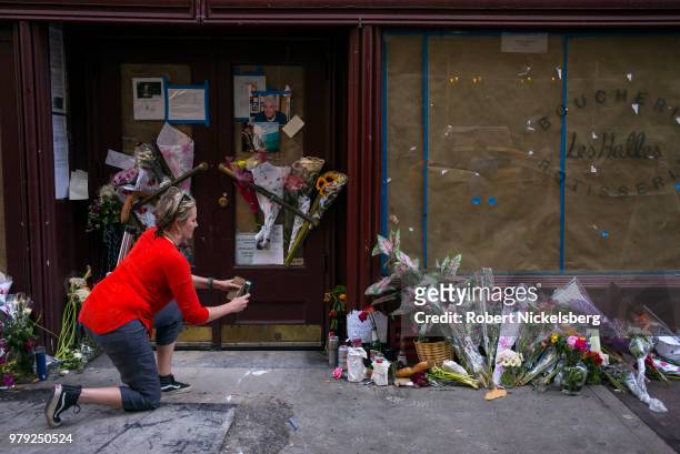 Woman takes a photograph of flowers, notes and photographs left in memory of Anthony Bourdain at the closed location of Brasserie Les Halles where...
