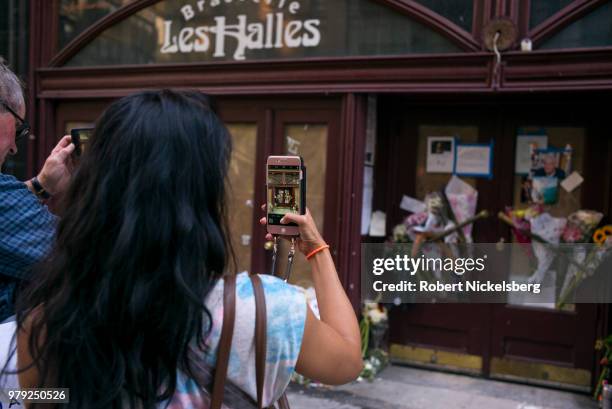 Woman takes a photograph of flowers, notes and photographs left in memory of Anthony Bourdain at the closed location of Brasserie Les Halles where...