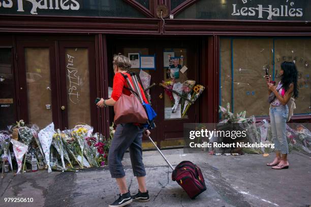 Woman takes a photograph of flowers, notes and photographs left in memory of Anthony Bourdain at the closed location of Brasserie Les Halles where...