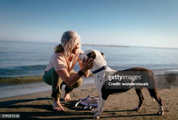 gelukkig volwassen vrouw kinderboerderij hond op het strand in de zomer - happy lady walking dog stockfoto's en -beelden