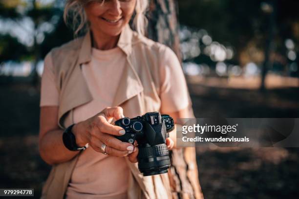 senior vrouw met behulp van de camera en het kijken naar foto's in de natuur - digitale spiegelreflexcamera stockfoto's en -beelden
