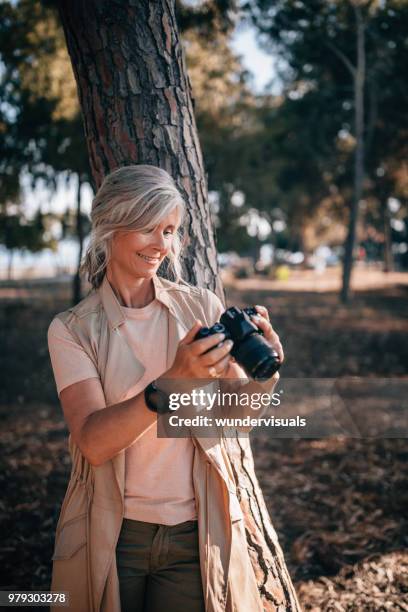 female mature photographer on summer vacations using camera in nature - old photographer imagens e fotografias de stock