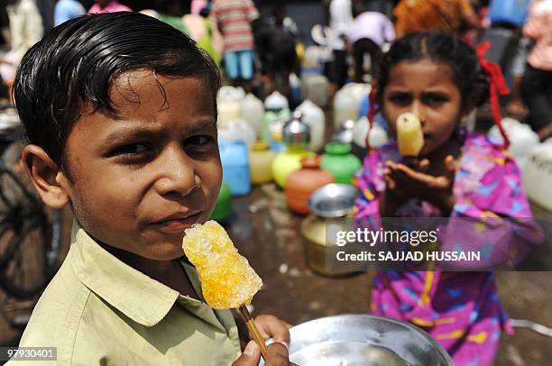 Indian children enjoy ice lollies as they wait for their mothers to fill containers with drinking water in Mumbai on World Water Day March 22, 2010....