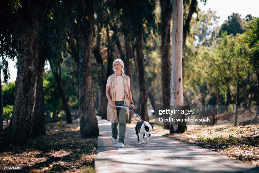 Smiling senior woman walking with pet dog in park