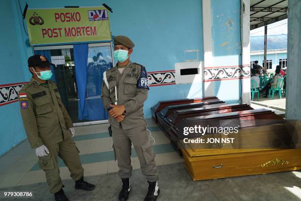 Local government officials guard coffins used for victims of a ferry that capsized on June 18, in front of a hospital morgue in Simalungun, in the...