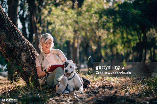 senior woman relaxing in nature with book and pet dog - dog relax imagens e fotografias de stock