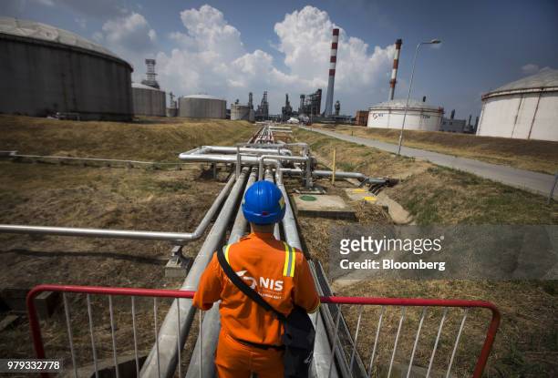 An employee walks across an oil storage tank backdropped by oil cracking towers at the Naftna Industrija Srbija AD oil refinery, operated by OAO...