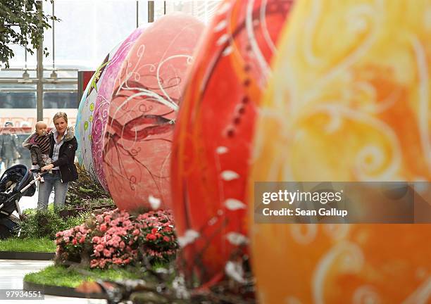 Woman holds her baby as she walks among giant Easter eggs coloured in the numerical progression of colours within the colour spectrum at the Arkaden...