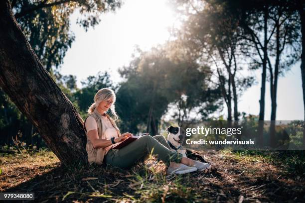 gelukkig volwassen vrouw ontspannen in de natuur met hond en boek - happy lady walking dog stockfoto's en -beelden