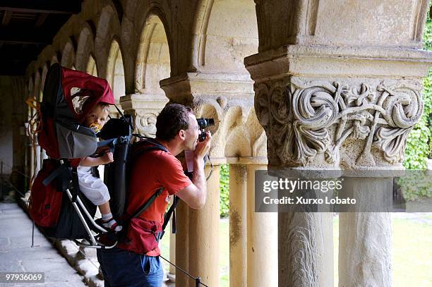 A tourist with his son hanging in his backpack makes a photo to Cloister of the Collegiate church of Santillana , Way of saint James, Cantabria...