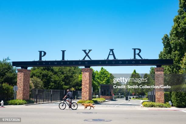 Man rides his bicycle and walks his dog past the entry gates at the headquarters of Pixar Animation Studios in downtown Emeryville, California, with...