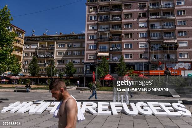 Pedestrian walks past block letters reading "#with refugees" on June 20 on World Refugee Day, in downtown Pristina.