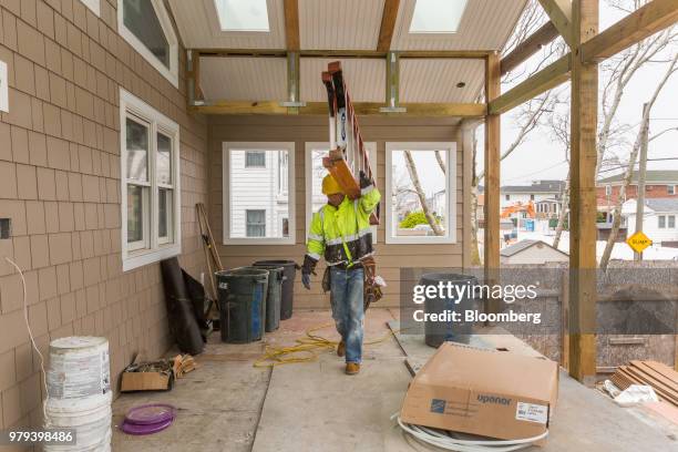 Worker carries a ladder to install a gutter during construction of a home designed to withstand extreme weather in the Breezy Point neighborhood of...