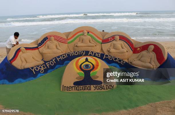 Sand artist Sudarsan Patnaik gives final touches to a sand sculpture depicting the message "yoga for harmony & peace next to Russian President...