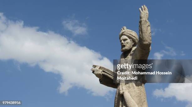 statue monument of persian poet ferdowsi with raised hand and holding book against cloudy sky, hamadan, iran - hamadan fotografías e imágenes de stock