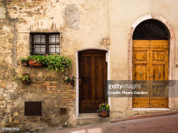 italian architecture of doors in weathered wall on street slope, san gimignano, tuscany, italy - san gimignano stock pictures, royalty-free photos & images