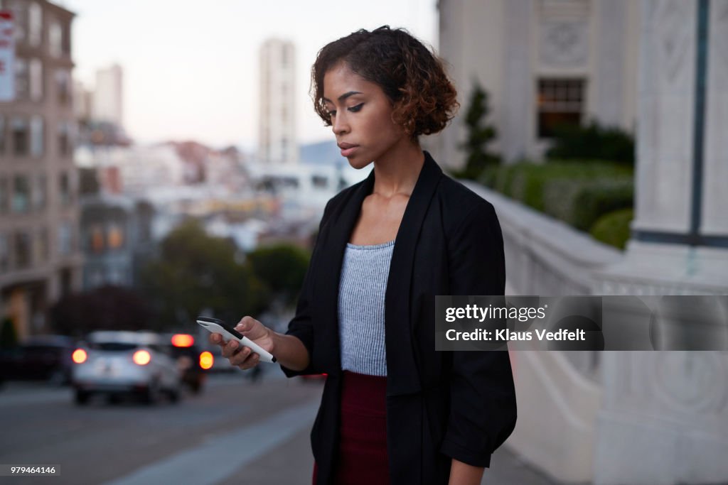Businesswoman checking phone while on the street in the evening