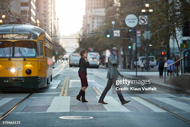 businesspeople walking on pedestrian crossing, while talking on smartphone - san francisco street stockfoto's en -beelden