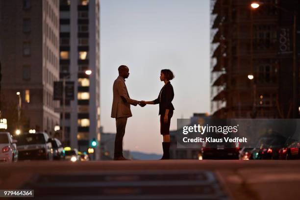 businessman and businesswoman standing on san francisco street and making handshake at night - angesicht zu angesicht stock-fotos und bilder