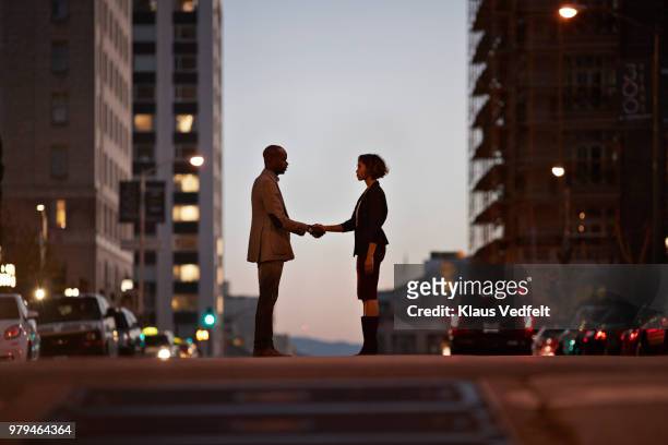 businessman and businesswoman standing on san francisco street and making handshake at night - faccia a faccia foto e immagini stock