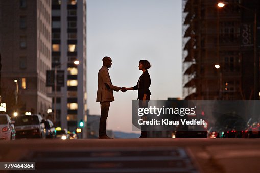 Businessman and businesswoman standing on San Francisco street and making handshake at night