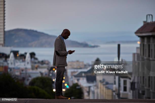 businessman checking phone while on the street in the evening - san francisco california street stock pictures, royalty-free photos & images