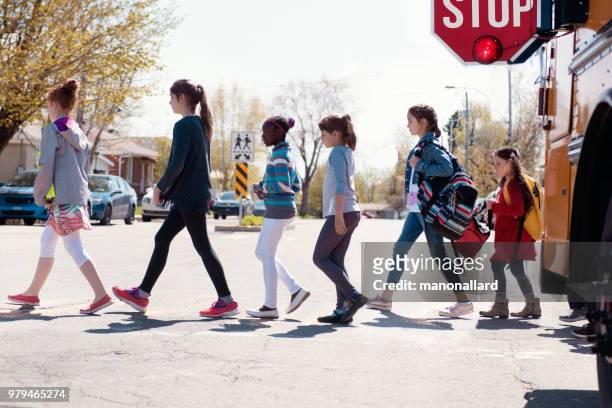 grupo multiétnico de la escuela primaria los niños salir de un autobús escolar en hacia fuera de la escuela. - crossing sign fotografías e imágenes de stock