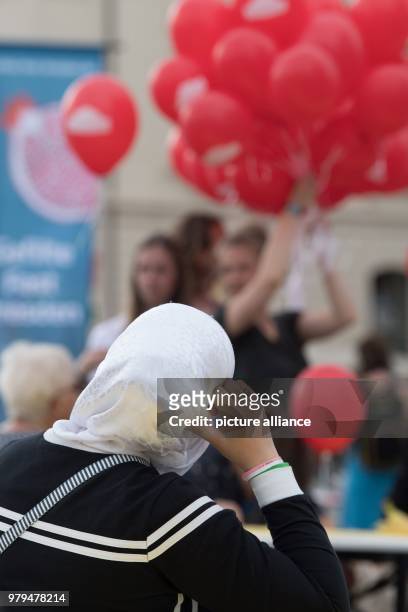 June 2018, Germany, Dresden: A woman with a headscarf sits at a table on the occasion of the event 'Gastmahl fuer alle' at the Neumarkt square....