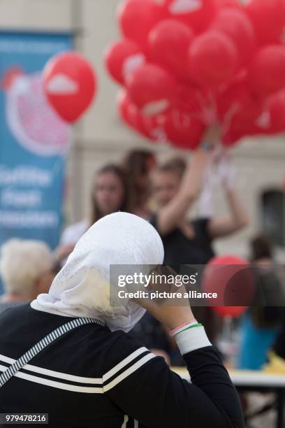 June 2018, Germany, Dresden: A woman with a headscarf sits at a table on the occasion of the event 'Gastmahl fuer alle' at the Neumarkt square....