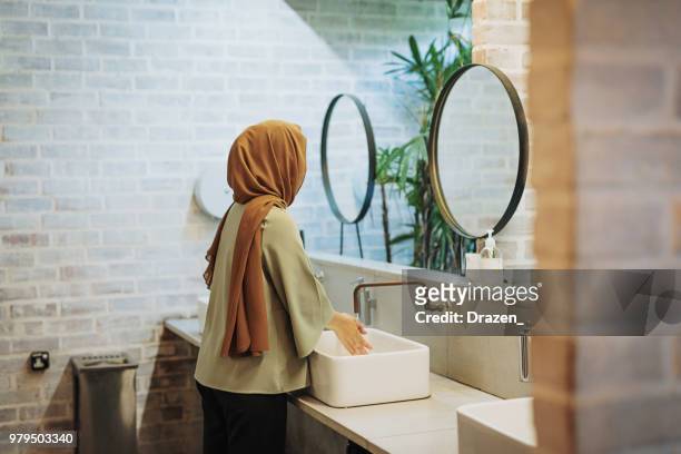 muslim woman with fixing hijab in restroom - vintage hand mirror stock pictures, royalty-free photos & images