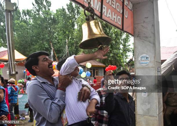 Hindu devotee helps a kid in ringing the bell as a mark of prayer during the annual Hindu festival at the Kheer Bhawani Temple in Ganderbal district,...