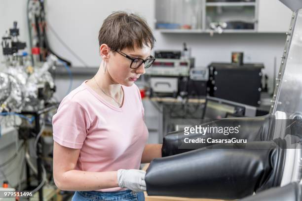young female researcher using glove box for measuring transient photocurrent in organic semiconductors - glove box stock pictures, royalty-free photos & images