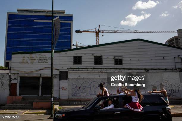 People ride in a vehicle moving past a shuttered animal clinic and a newly constructed building in the Las Mercedes neighborhood of Caracas,...