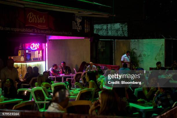 Customer sit on the patio of a bar at night in the Las Mercedes neighborhood of Caracas, Venezuela, on Friday, June 8, 2018. Las Mercedes, the...