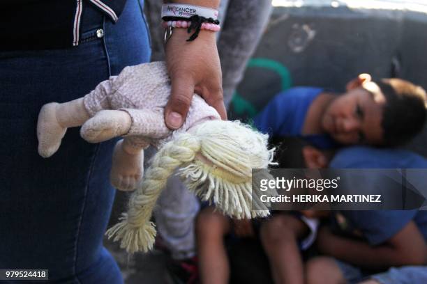 Mexican woman holds a doll next to children at the Paso Del Norte Port of Entry, in the US-Mexico border in Chihuahua state, Mexico on June 20, 2018....