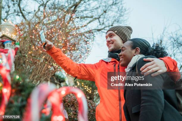 het interracial verliefde paar, de mooie zwarte jonge vrouw en een knappe jongeman, maken selfie met kerstverlichting en plezier in de koude winterdag in brooklyn, new york. - black christmas stockfoto's en -beelden