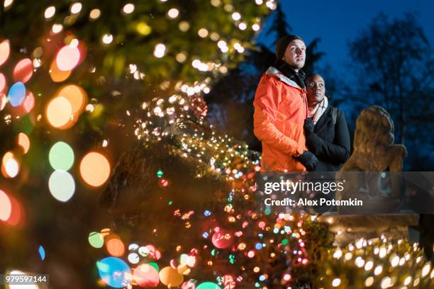 het interracial verliefde paar, de mooie zwarte jonge vrouw en een knappe jongeman, hugs omgeven door kerstverlichting en plezier in de koude winterdag in brooklyn, new york. - black christmas stockfoto's en -beelden