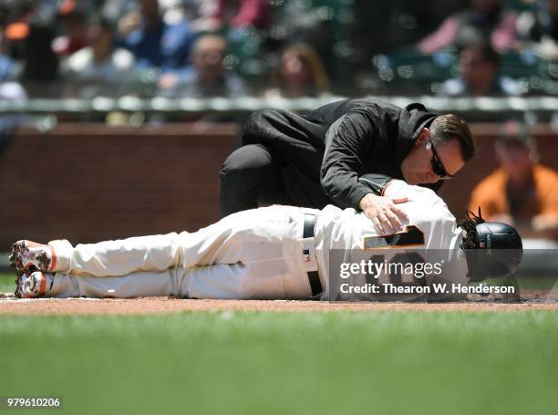 Alen Hanson of the San Francisco Giants is looked at by trainer Dave Groeschner after Hanson fouled a pitch off the top of his knee against the Miami...