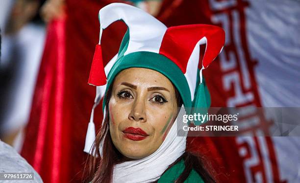 An Iranian woman football supporter wearing a jester's hat with her country's colours stands before a national flag during a screening of the Russia...