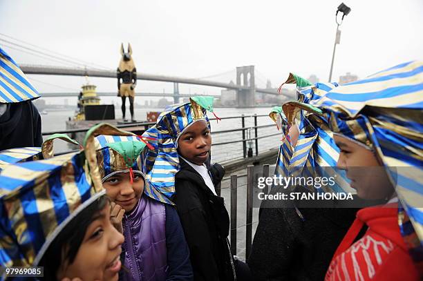 New York City school students wearing "King Tut" hats gather to see a 25-foot tall, 7-ton replica statue of the Egyptian god Anubis on a barge near...