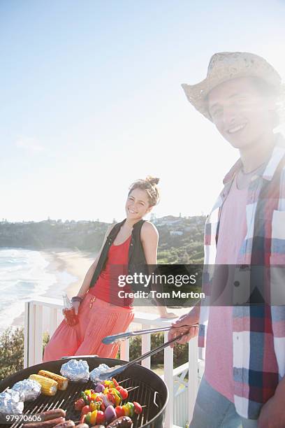 man and woman tending barbecue with ocean in background - australian bbq stockfoto's en -beelden