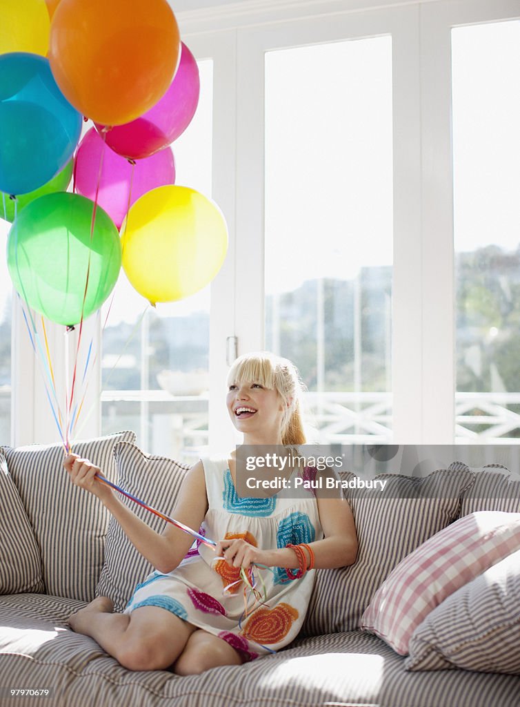 Woman holding balloons on sofa in living room