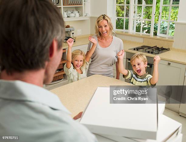 man arriving in domestic kitchen with pizza boxes and family cheering - hungrybox stock pictures, royalty-free photos & images