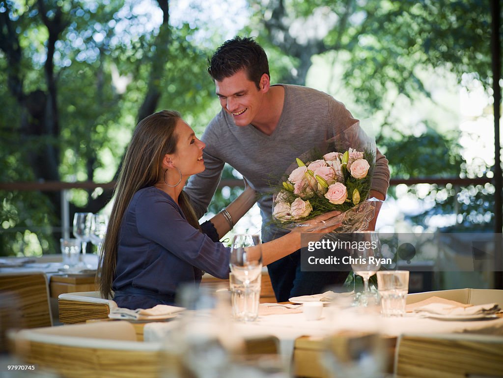 Man giving flowers to woman at restaurant table