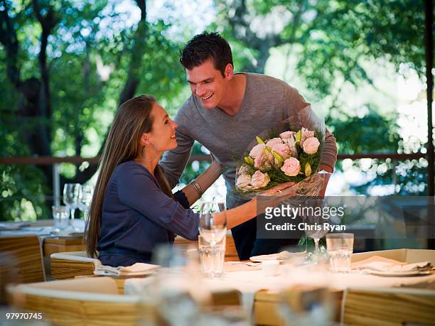 man giving flowers to woman at restaurant table - day celebration dinner arrivals stockfoto's en -beelden
