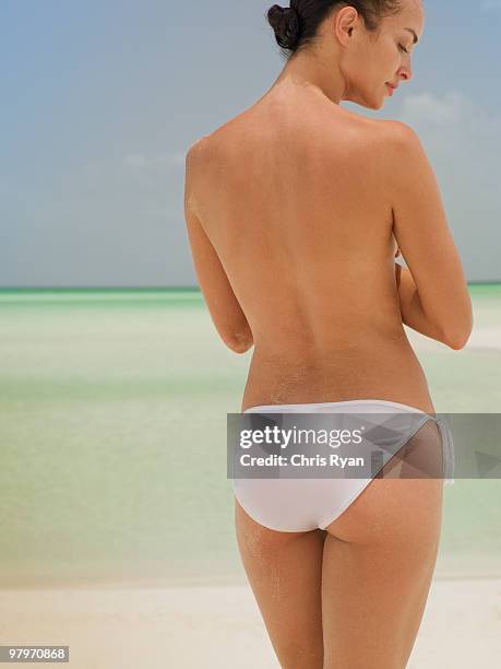 woman with bare chest and bikini bottoms standing on beach - bare bottom women stockfoto's en -beelden